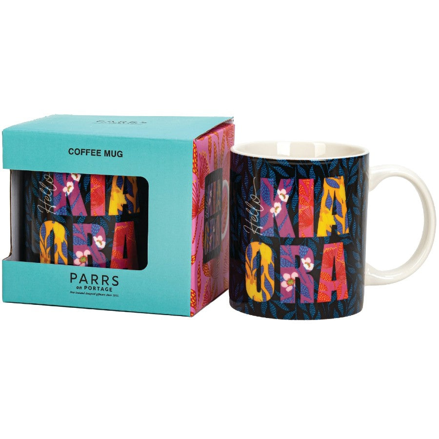 Colorful coffee mug with 'Mia Cara' design next to its packaging on a white background