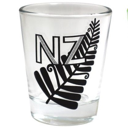 A clear glass shot glass featuring a black printed design of the letters 'NZ' stylized with a fern leaf.
