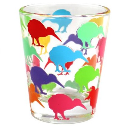A clear glass shot glass decorated with a colorful pattern of kiwi bird silhouettes in red, blue, green, purple, orange, and pink, set against a plain white background.